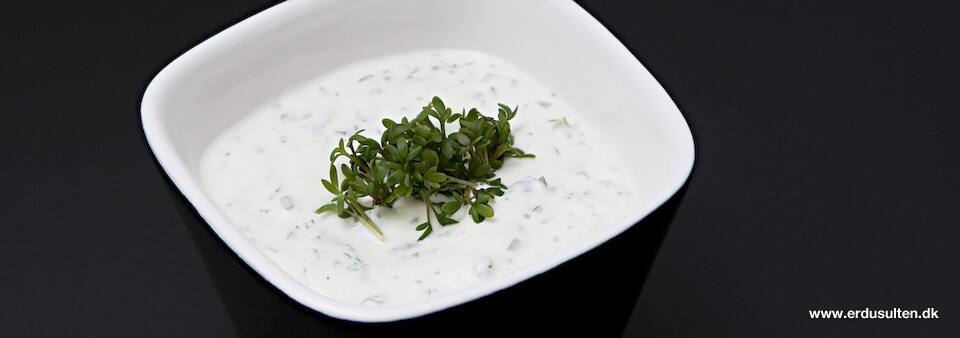 Cremet urtecreme i hvid skål med frisk karse, purløg, persille og basilikum på toppen, mørk baggrund.
