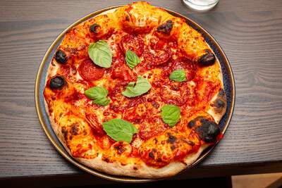 Sprød gylden pizza med boblende ost, pepperoni og friske basilikumblade samt tydeligt rød sauce.
