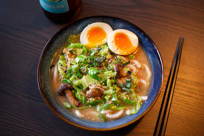 Ramen med tre svampe og bløde æggehalvdele i cremet bouillon, grønne forårsløg, sesam i dyb blå skål.