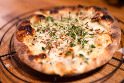 Gylden pizza med smeltet ost, sprøde kanter og grønne timianblade som topping.