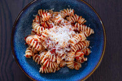 Al dente fusilli i krydret rød tomatsauce med friskrevet ost på blå tallerken.
