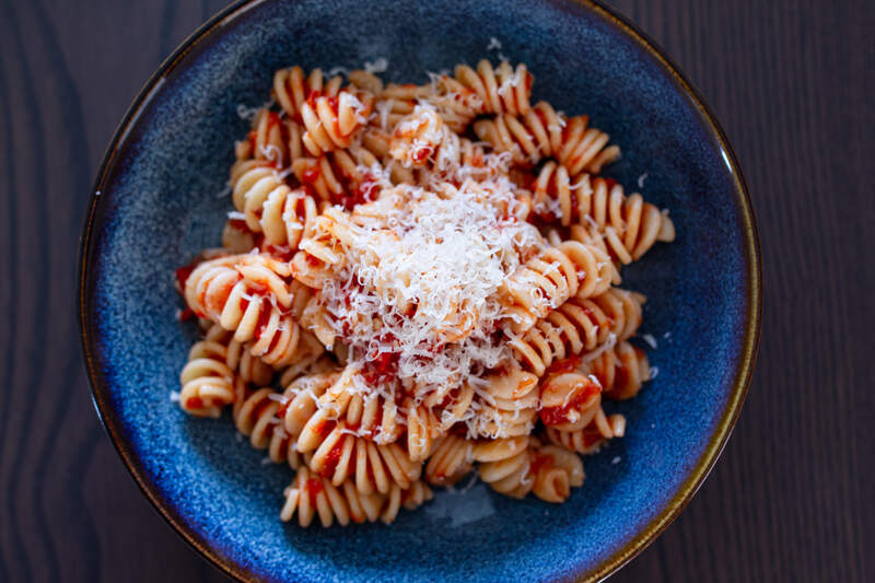 Al dente fusilli i krydret rød tomatsauce med friskrevet ost på blå tallerken.