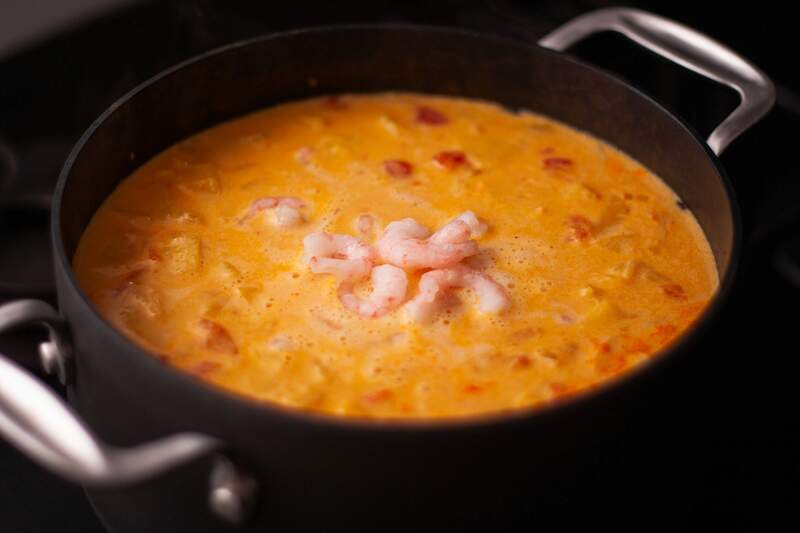 Karrysuppe med rejer og fersken, cremet gylden-orange, med små røde chili-flager og hvide rejer som topping.