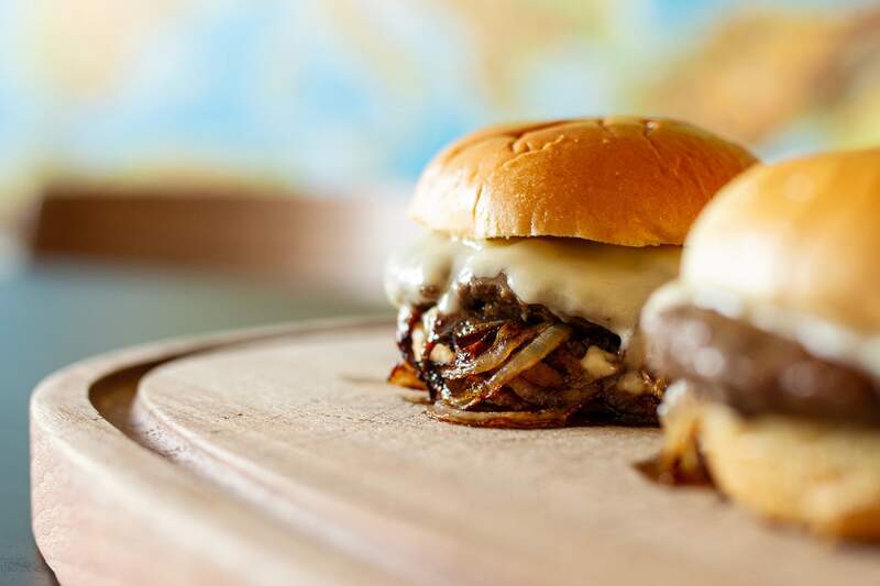 Saftig Oklahoma løg smash-burger med smeltet ost og karamelliserede løg, glat gylden top på træskærebræt.