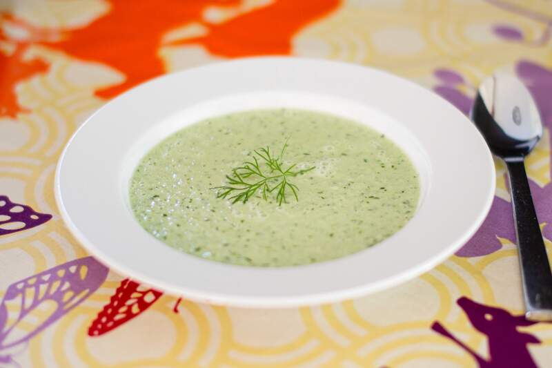 Lysegrøn, cremet kold agurksuppe med græsk yoghurt og frisk dild, pyntet med dillkvist i en hvid skål.
