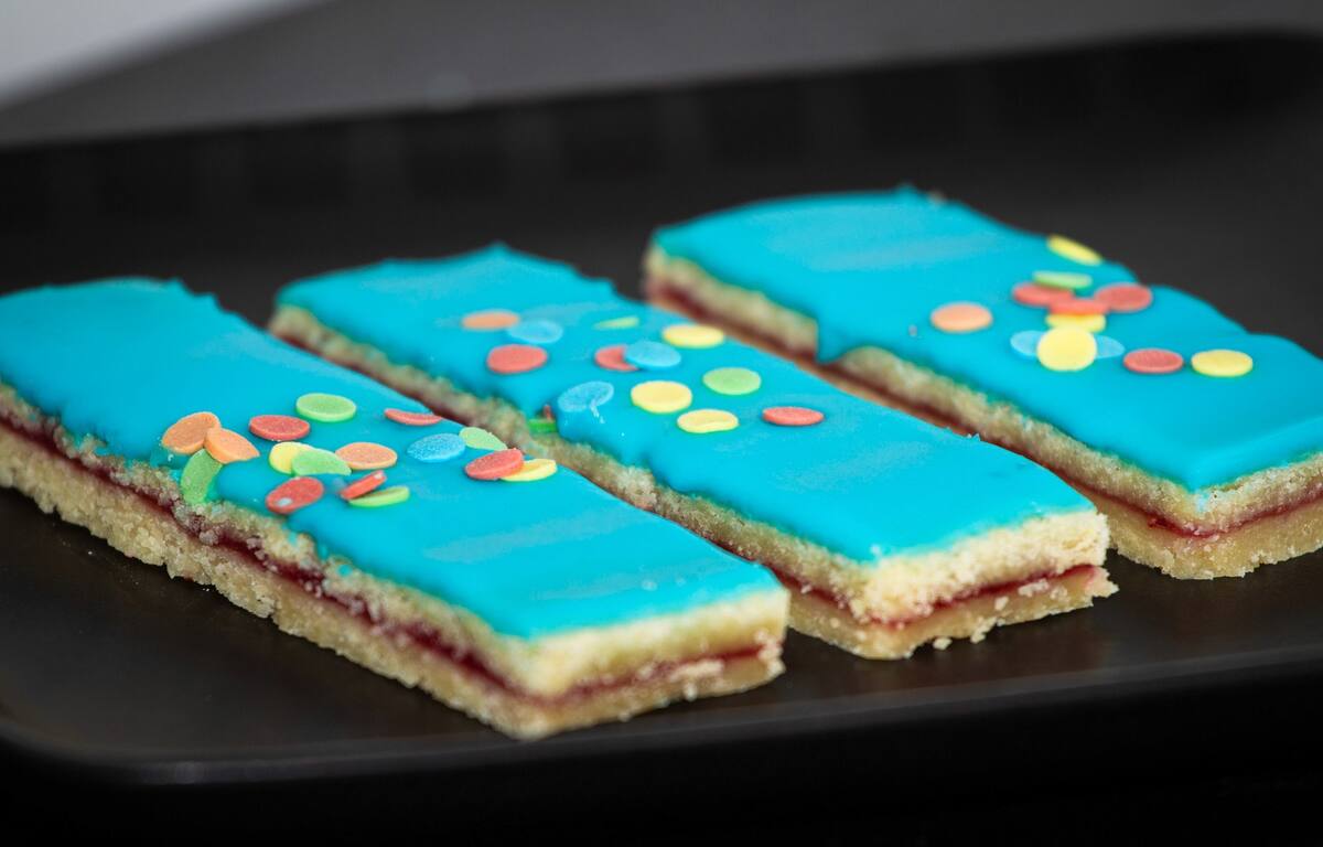 Tre hindbærsnitter med blå glasur, sprøde kanter, farverige tivolidrys og syltetøjslag.