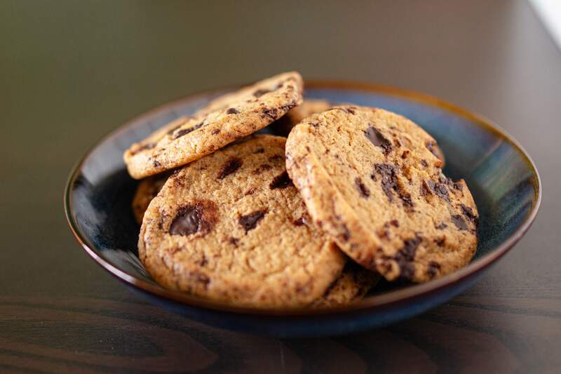 Gyldne cookies med store chokoladestykker ligger stablet på en blå tallerken, sprøde kanter og blød midte.