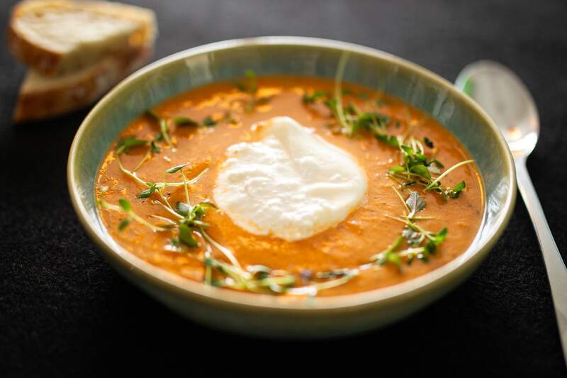 orange tomatsuppe i grøn skål med burrata midt, timian og spirer som pynt