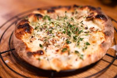 Gylden pizza med smeltet ost, sprøde kanter og grønne timianblade som topping.
