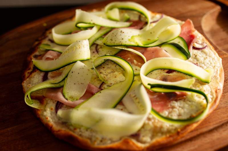 Grønne squashstrimler og tynde skiver parmaskinke på gylden sprød pizza med cremet hytteost.