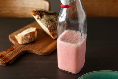 Lyserød jordbær-banan smoothie i glasflaske med bobler og træbord i baggrunden