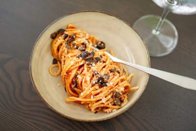 Orange spaghetti i dyb skål med skiver af oliven, ansjoser, kapers og let revet ost.