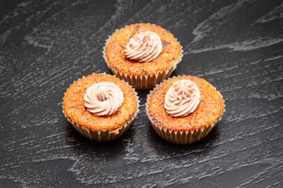 Tre bananmuffins med lysebeige frosting, sprøde kanter og saftig, gylden midte på sort bord.