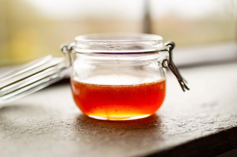 Glimtende chili-honning i gennemsigtig glasbeholder; orange rød væske med små chiliflager.